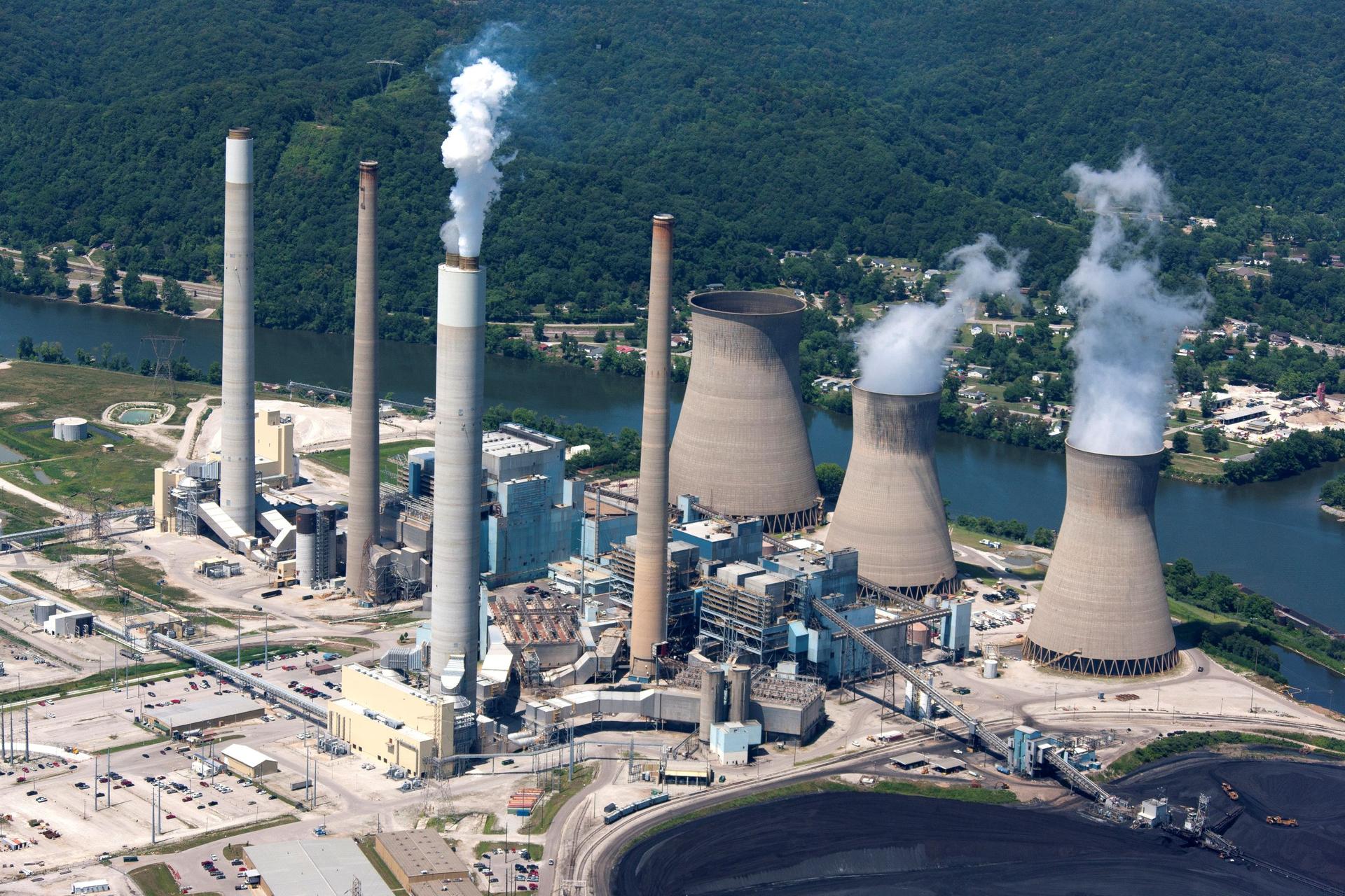 Aerial view of smoke coming from a coal-fired power plant on the banks of a river.